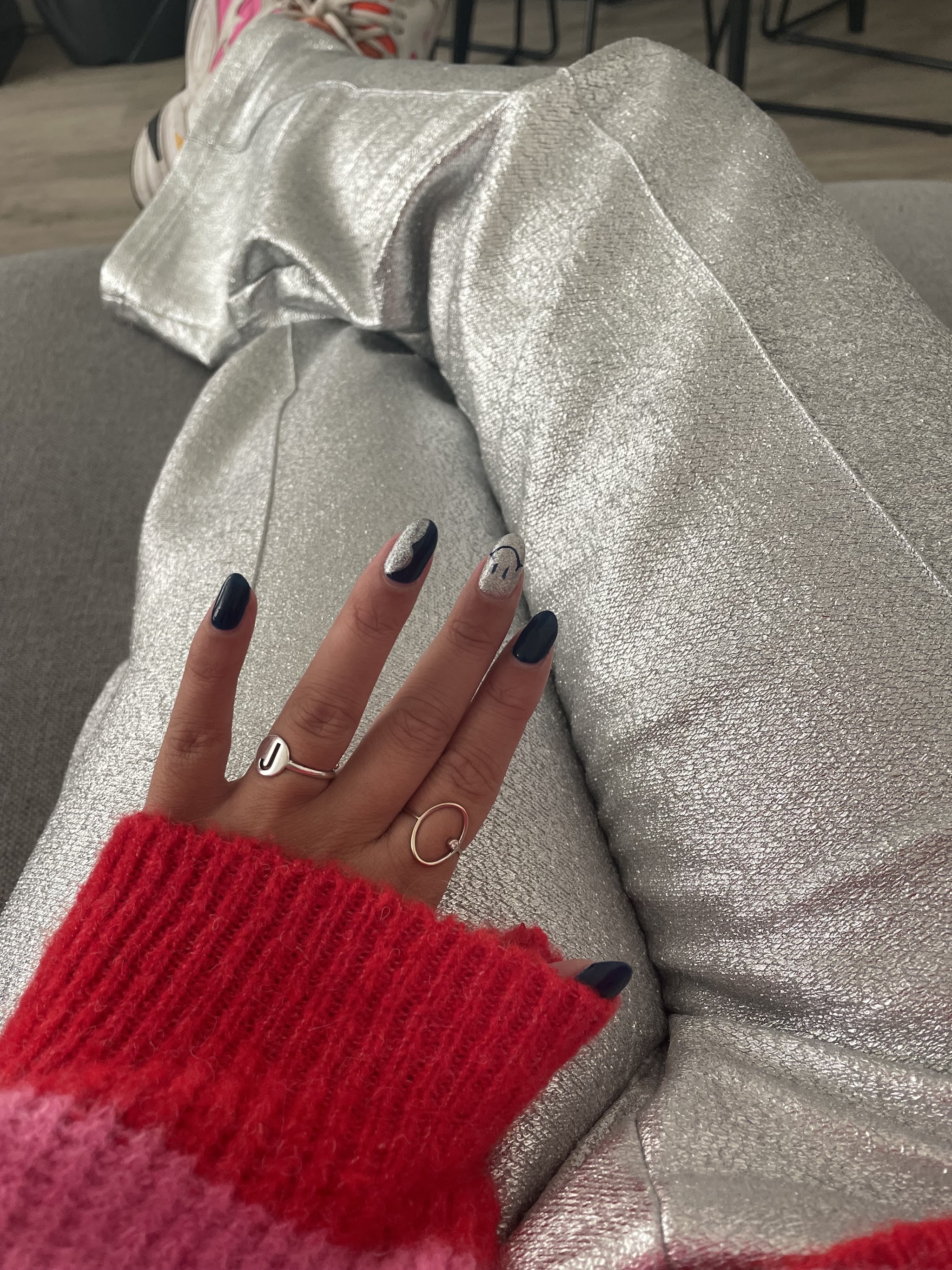 Donkerblauwe nagels met glitter en een smiley, met een rode gebreide mouw