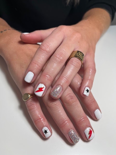 Witte nagels met rode bliksemschichten, zwarte sterren en een glitternagel