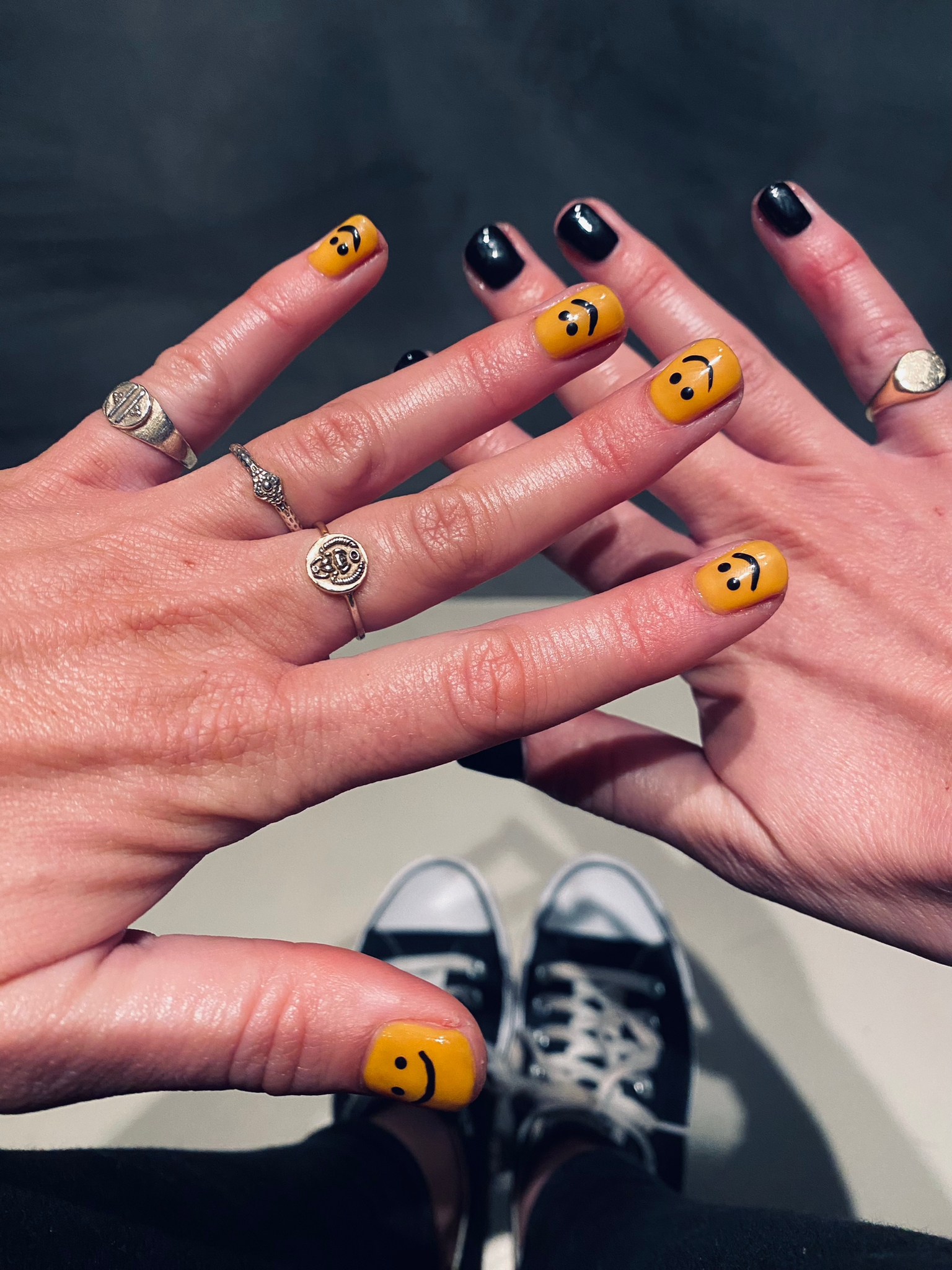 Twee handen met gele smiley-nagels in combinatie met zwart en donkerblauw