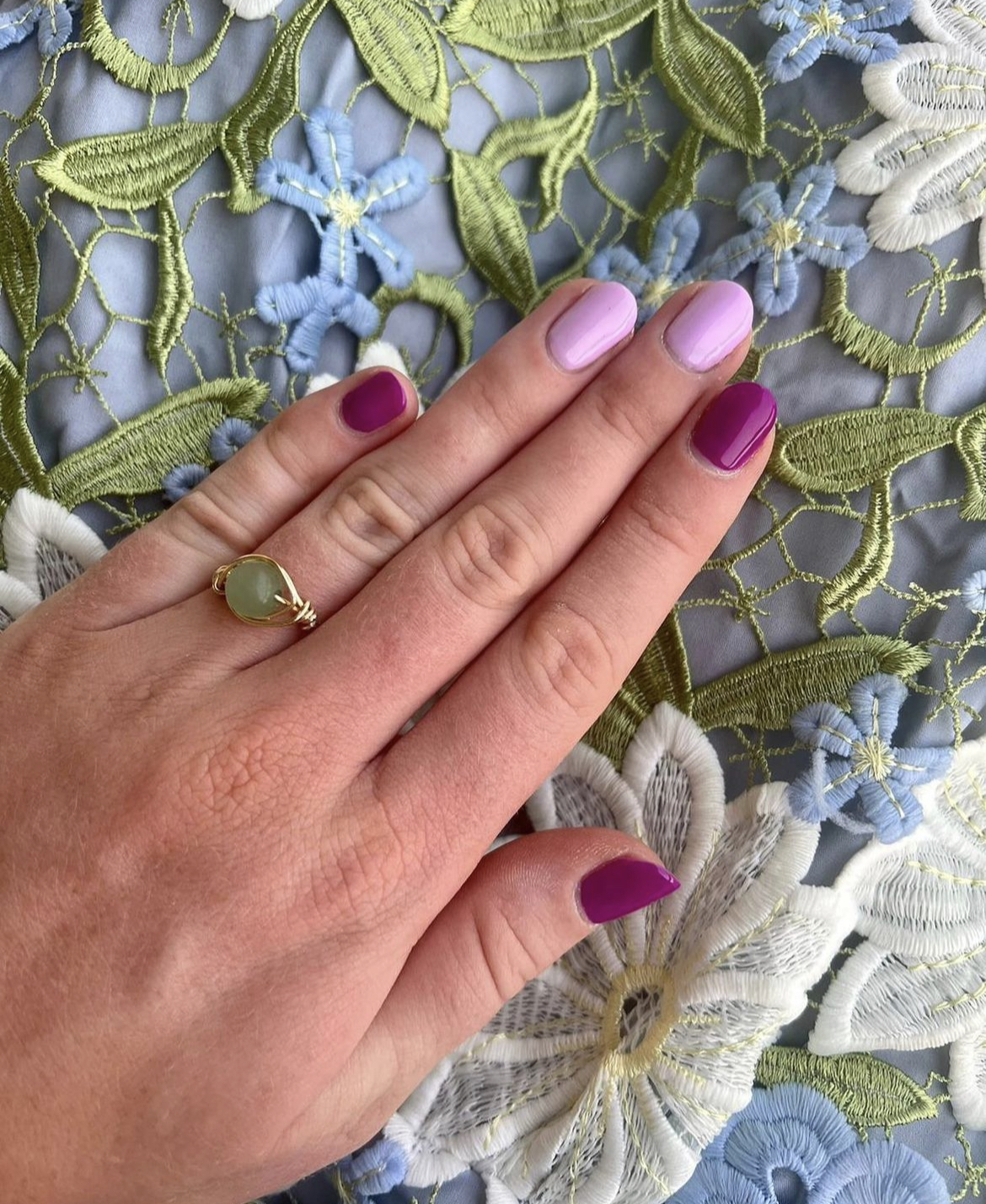 Hand met lila en magenta nagels op een stof met bloemenkant